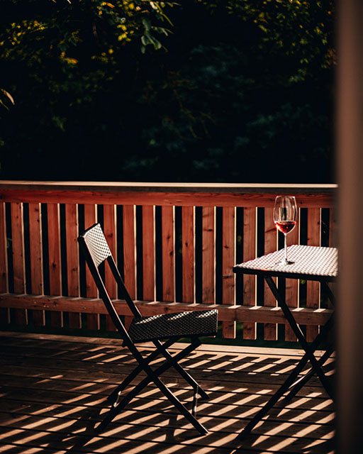 Фотография уютной веранды с плетеной мебелью и бокалом вина на столе.