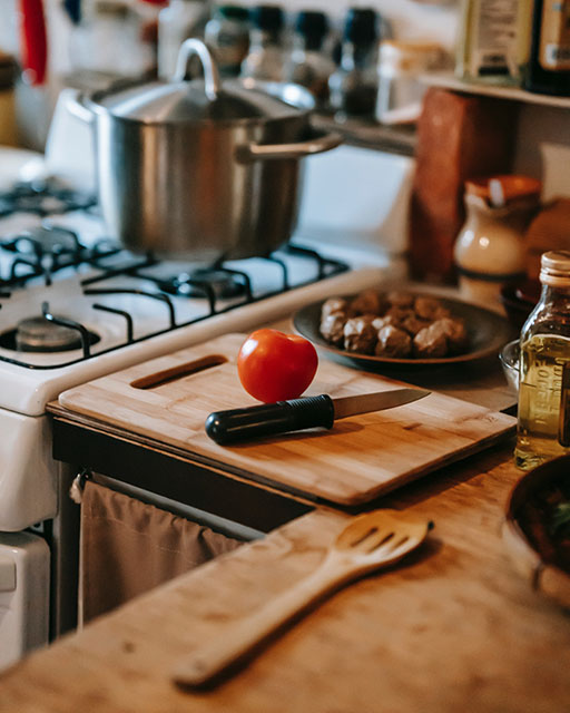 Фотография кухни: газовая плита с кастрюлей, разделочная доска, нож и помидор.